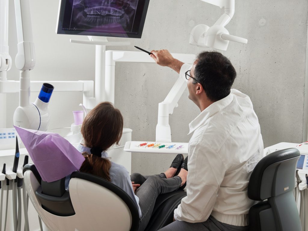 Dental patient in chair as dentist shows teeth x ray on screen