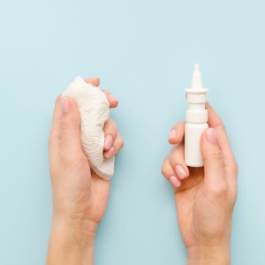 Hands holding tissue on the left and nasal spray on the right