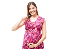 Pregnant woman brushes teeth while holding stomach