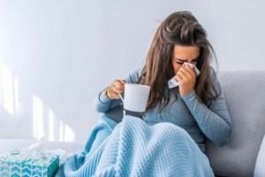 Sick woman holding mug and blowing her nose